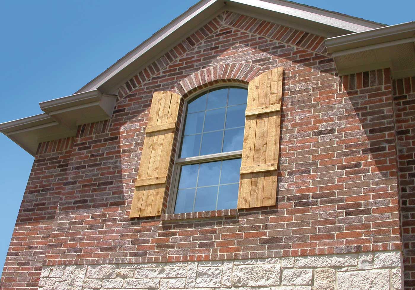 Brick building with arched window, wooden shutters, and blue sky.
