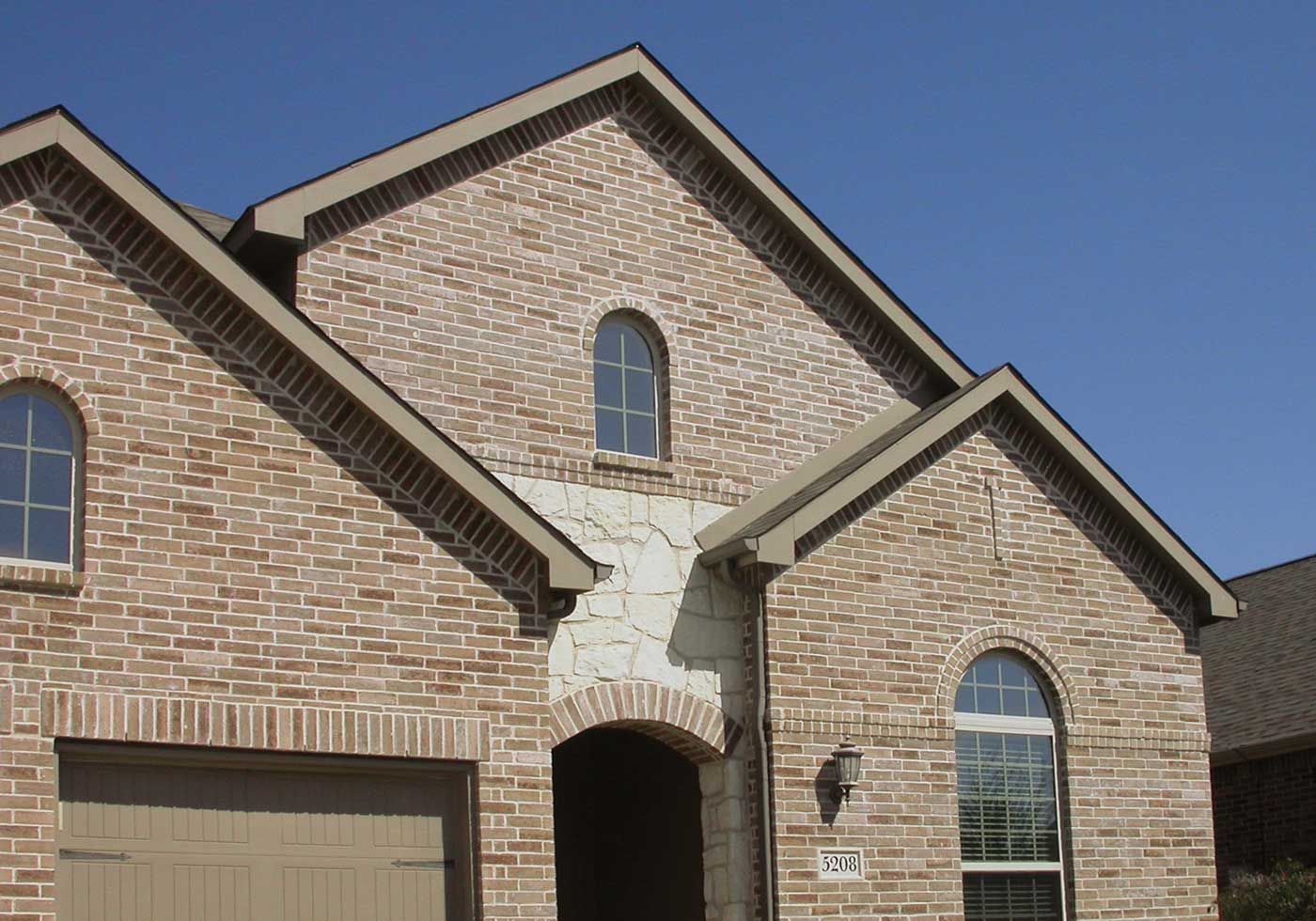 Brick house with multiple gables and arched windows, against a blue sky.