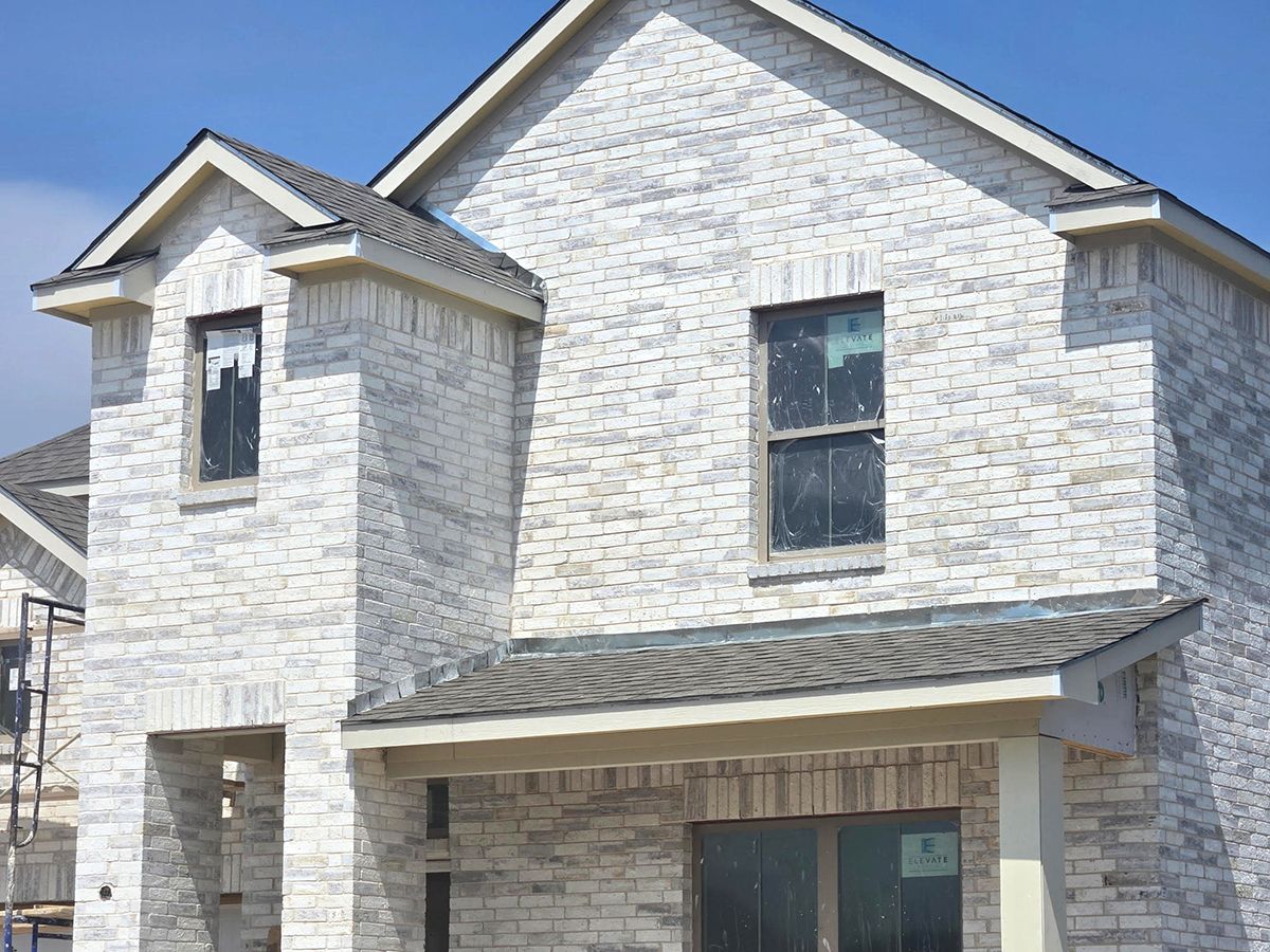 Two-story house with whitewashed brick exterior, dark windows, and gray roof.