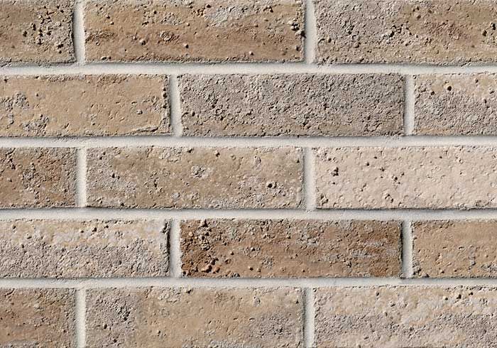 Close-up of a brick wall with varying shades of tan and brown bricks, white mortar lines.