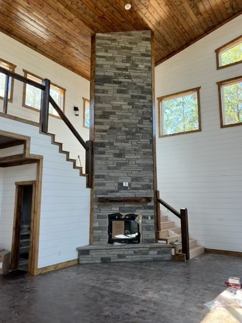 Stone fireplace in a modern home, wood ceiling and stairs, windows with natural light, open space.