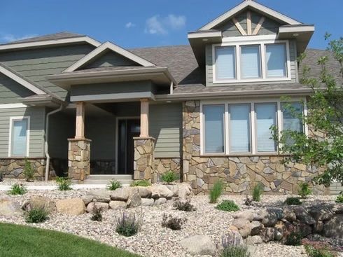 Green house with stone accents, front entrance, and landscaping under a blue sky.