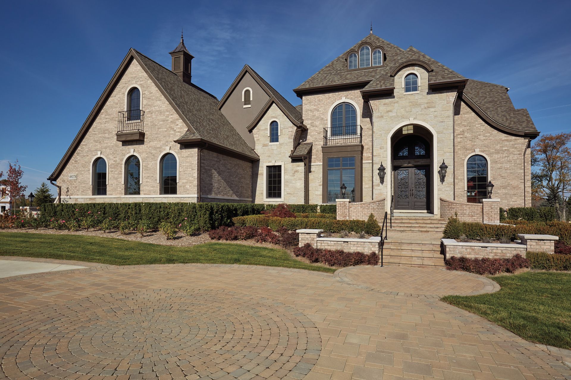 Brick house with arched windows and doorway, cobblestone driveway, and manicured landscaping.