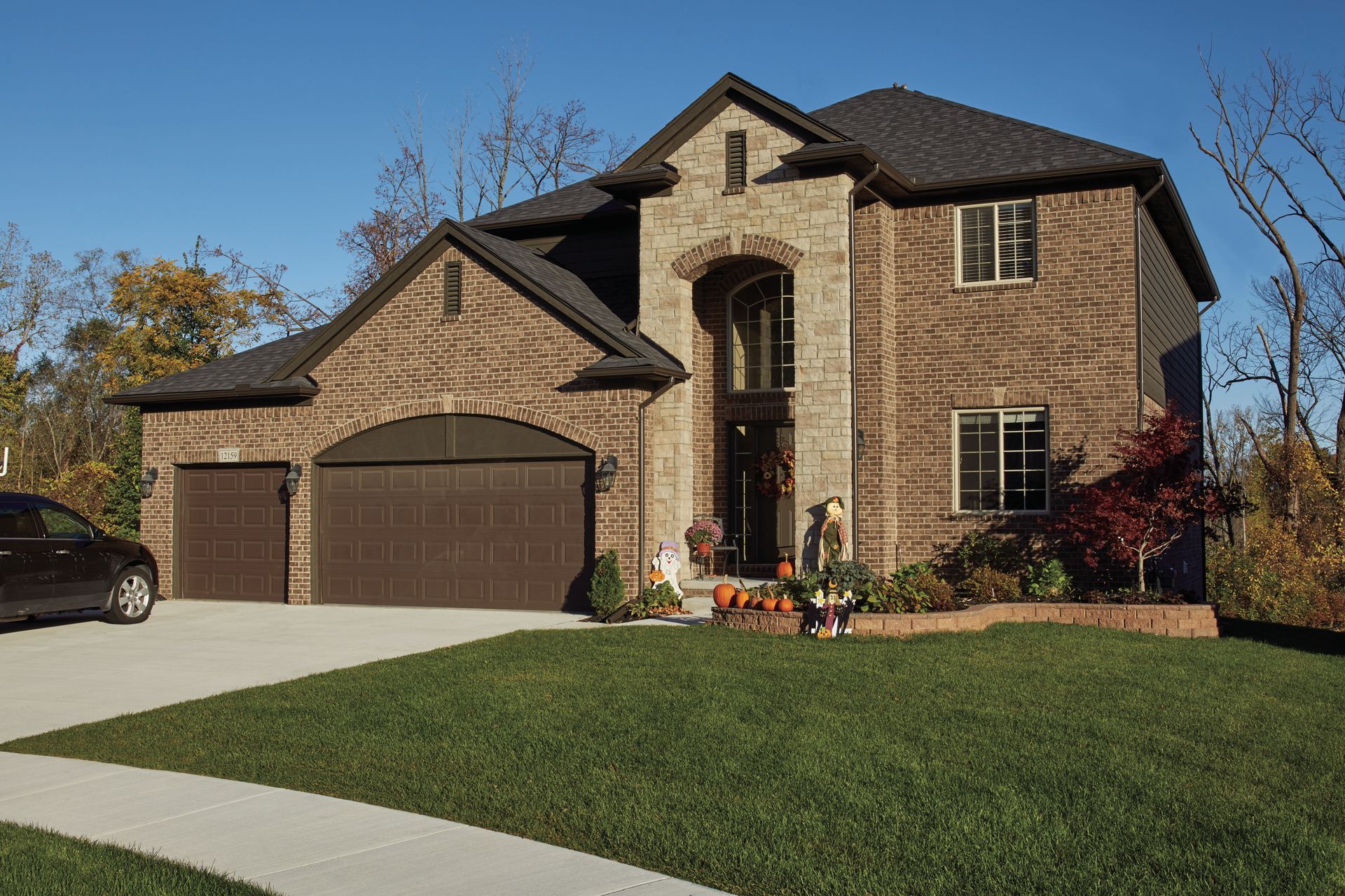 Brick house with arched garage, driveway, and front lawn. Car parked in the drive, with blue sky backdrop.