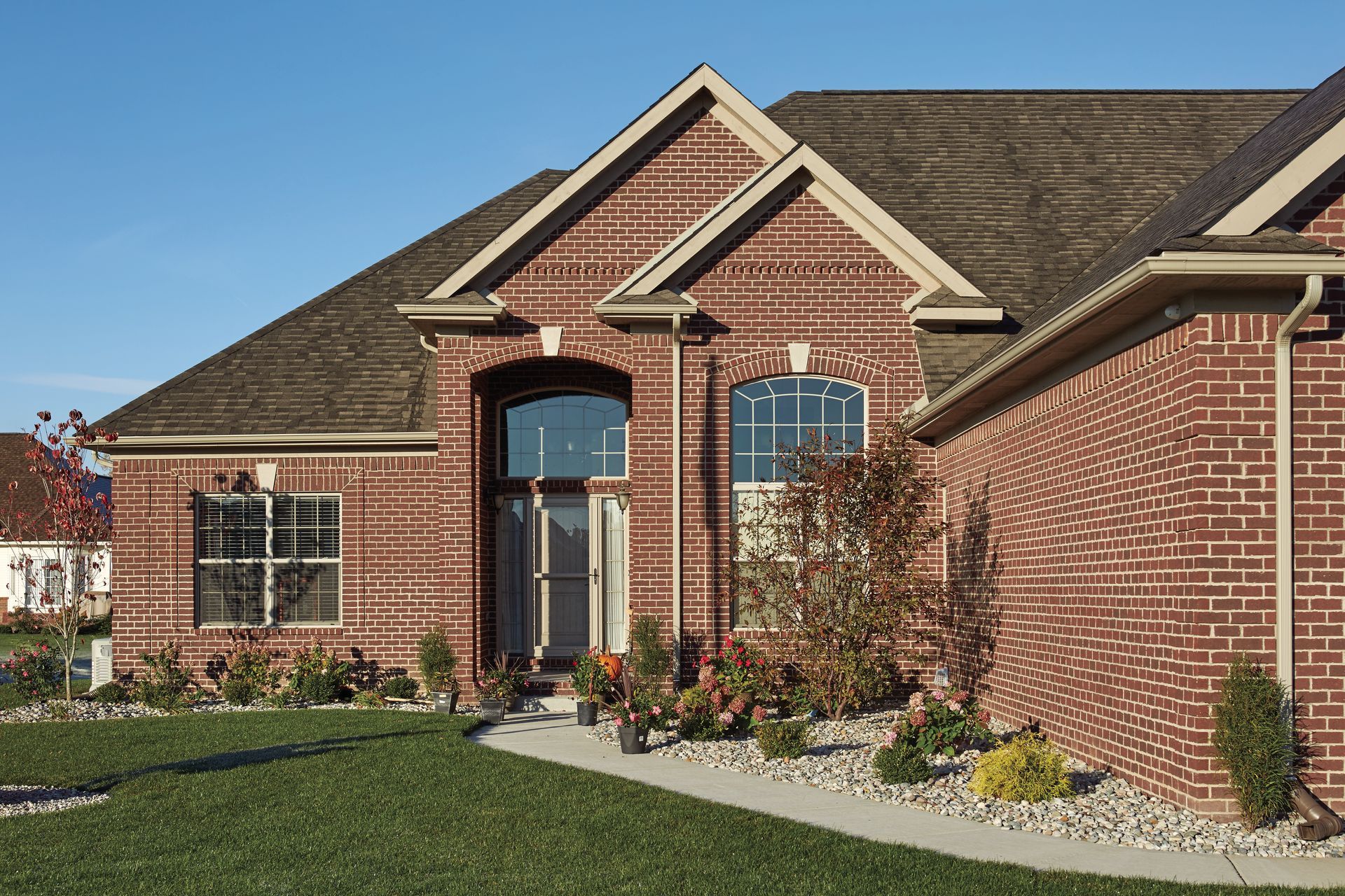 Red brick house with a dark brown roof and blue sky.
