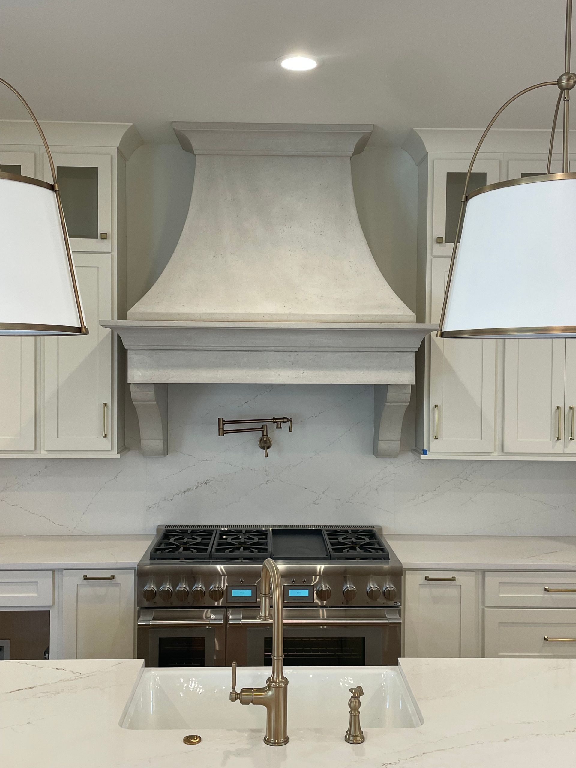 Kitchen with stainless steel stove, range hood, white cabinets, and pendant lights.