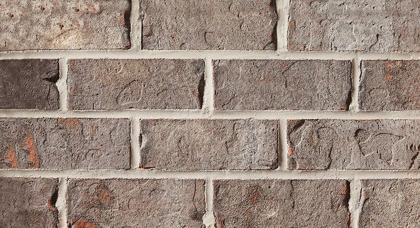 Close-up of a weathered brick wall with varying shades of gray, brown, and hints of red mortar.
