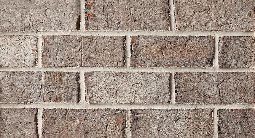 Close-up of a brick wall with gray mortar. The bricks are shades of brown and gray.