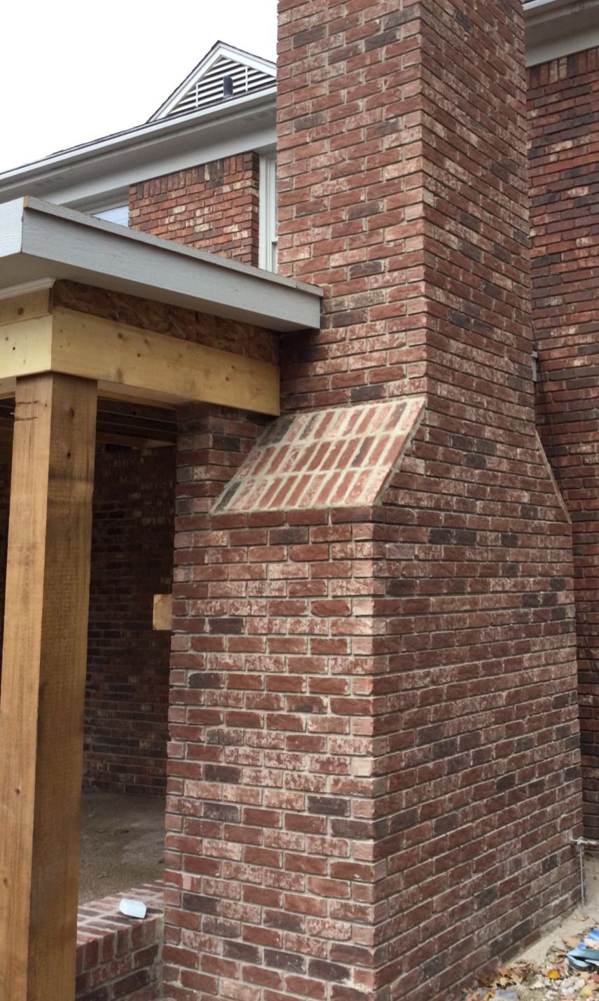 Brick chimney extending from a house with a covered porch; brown bricks.
