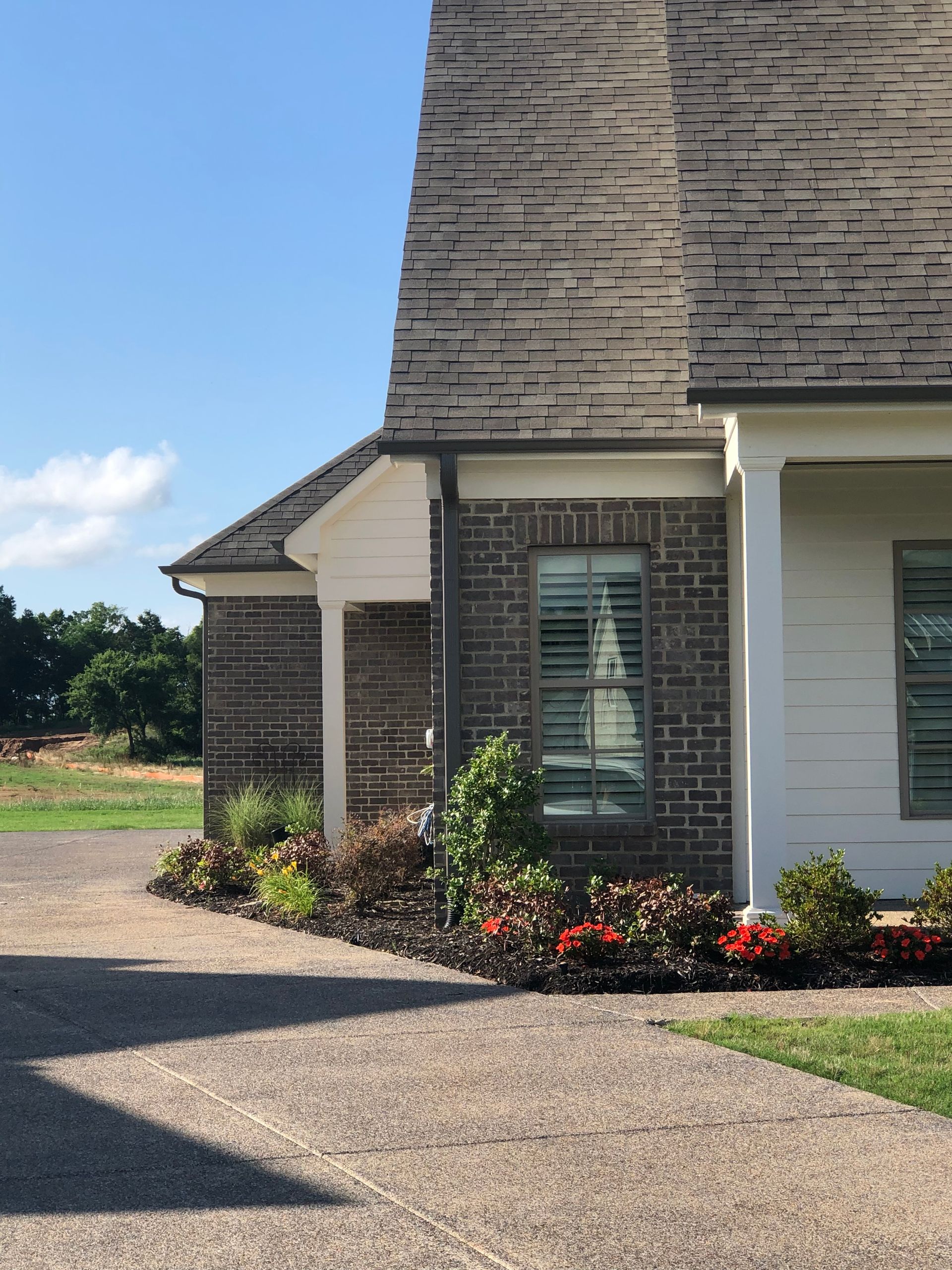 Exterior of a brick and white house with a dark gray roof. Landscaping in front. Blue sky.