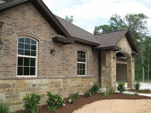 Brick house with brown roof and white-framed windows, surrounded by landscaping, under a cloudy sky.