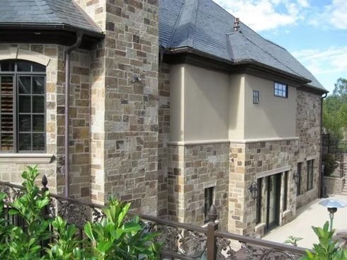 Stone house exterior with a dark roof and large windows.