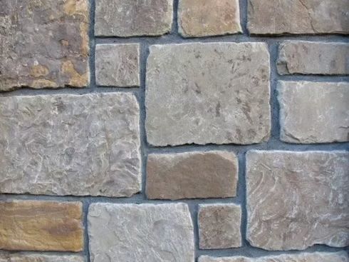 Stone wall, various sizes and shades of tan and gray blocks, with gray mortar.