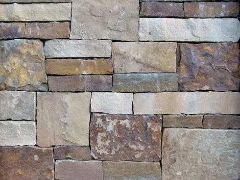 Stone brick wall with tan, brown, and gray rectangular blocks.