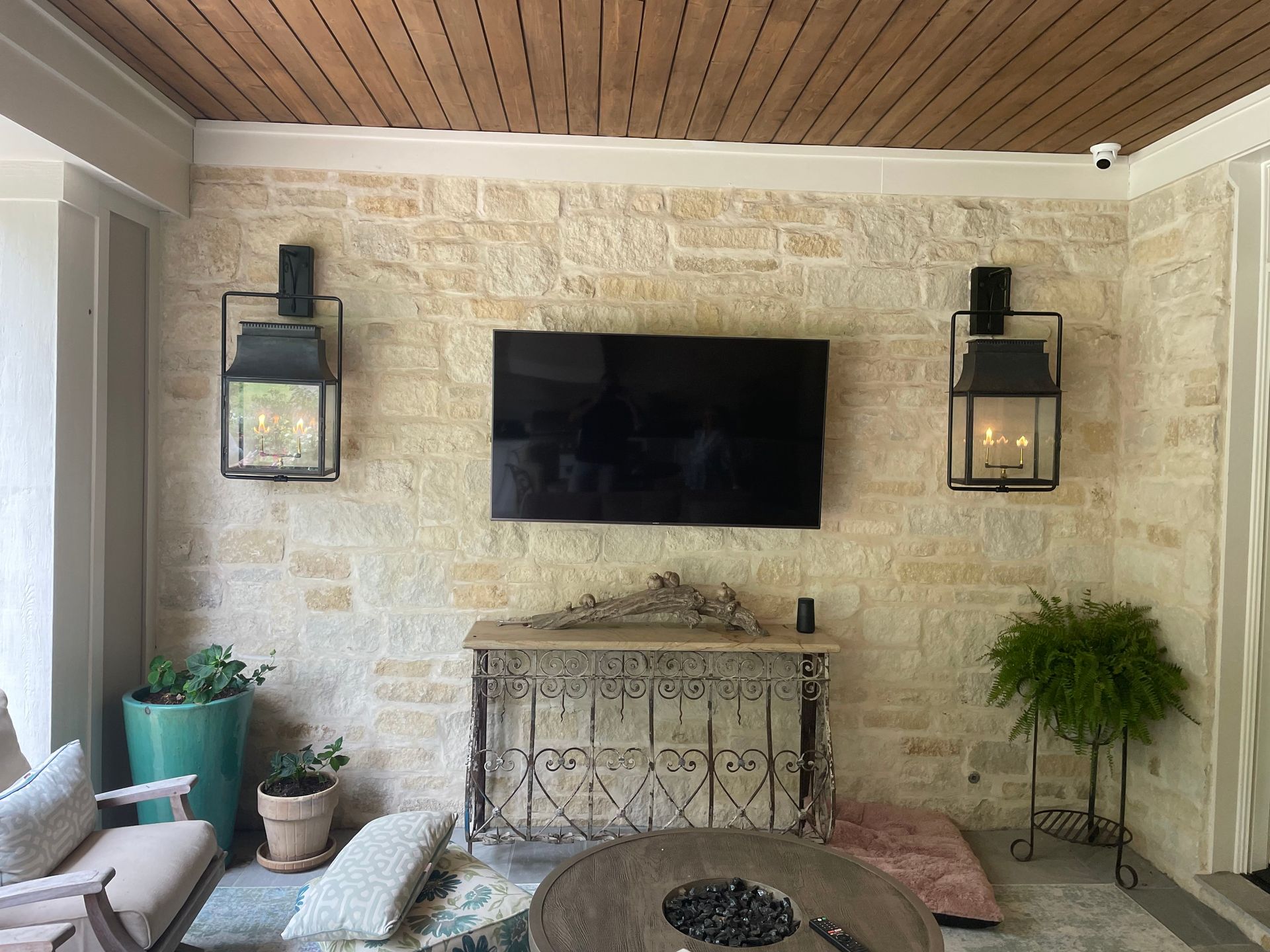 Outdoor patio with stone wall, TV, lanterns, and furniture.