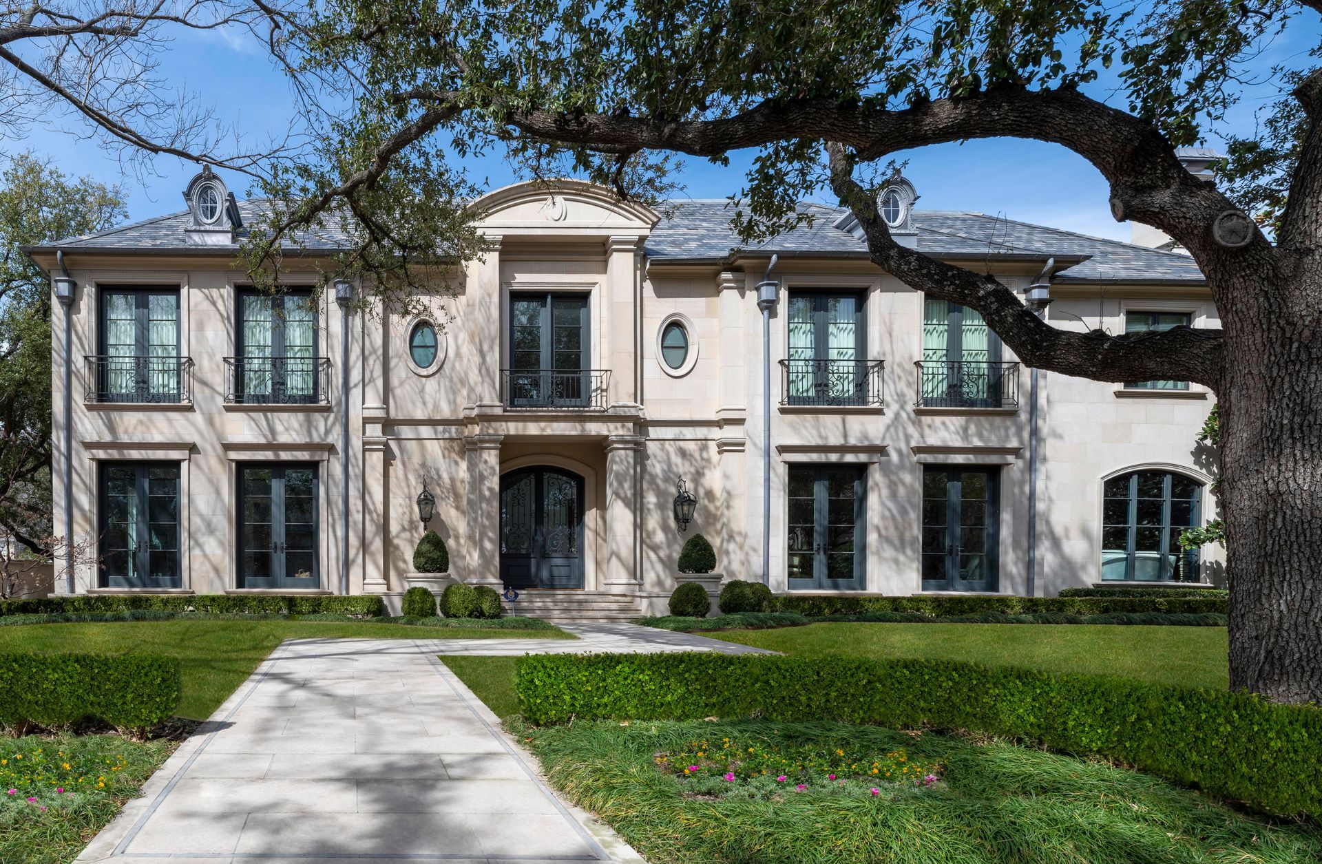 Elegant beige mansion with dark window frames and doors, centered on a manicured lawn.