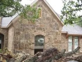 Stone facade building with arched window and a gabled roof. Tree branches in foreground.