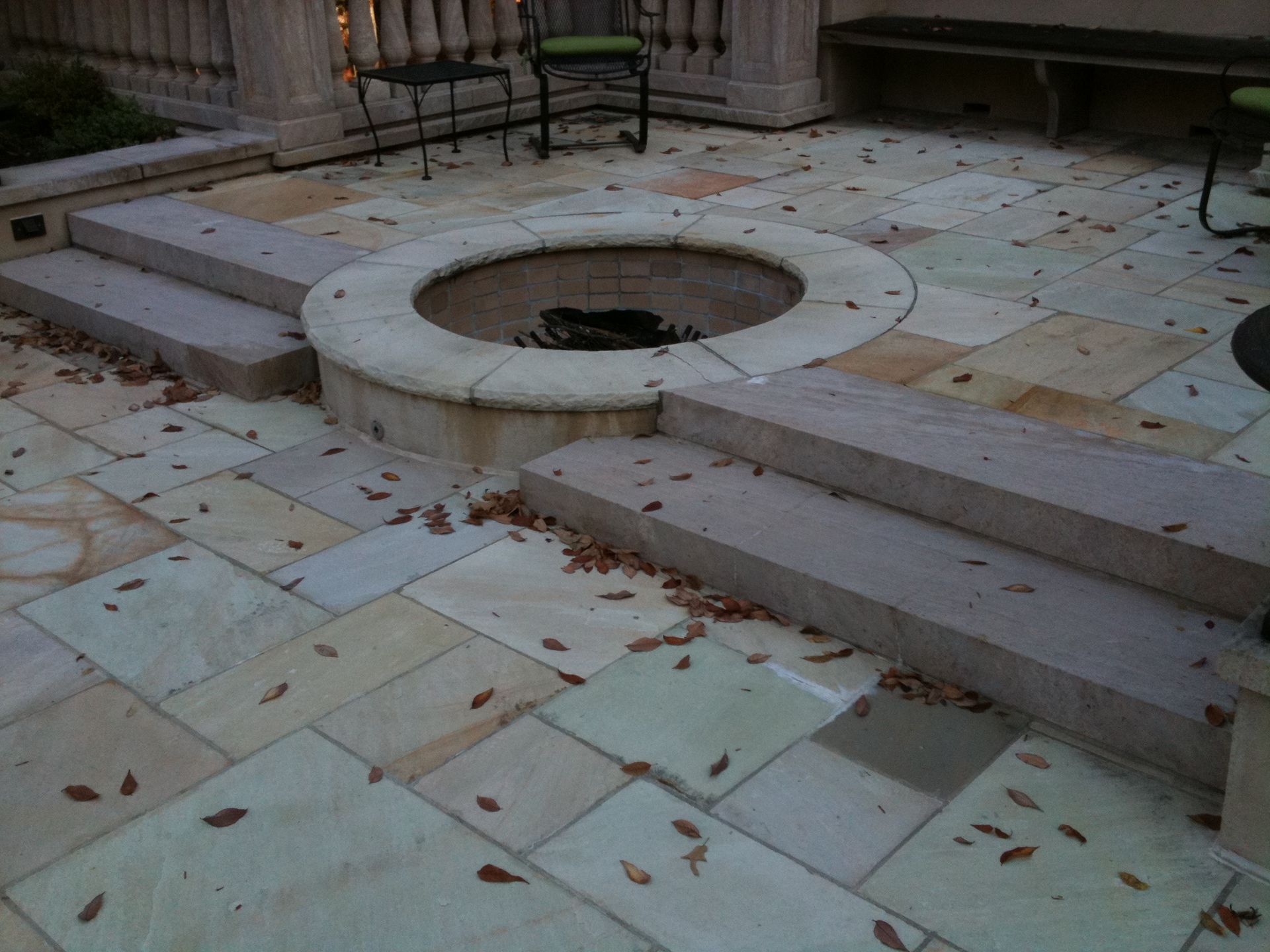 Outdoor patio with fire pit, stone steps, and flooring. Scattered leaves.