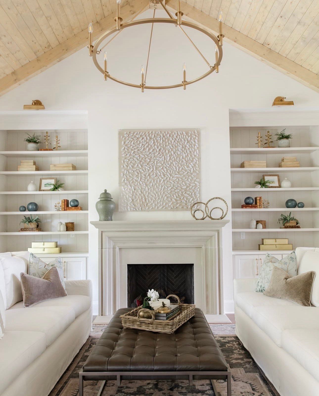 Living room with white sofas, fireplace, built-in bookshelves, and a large circular chandelier.