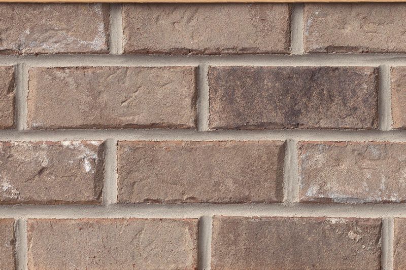 Close-up of a brick wall with tan, brown, and grey bricks and grey mortar.