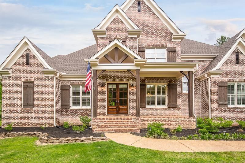 Brick home with brown shutters, porch, and a US flag.