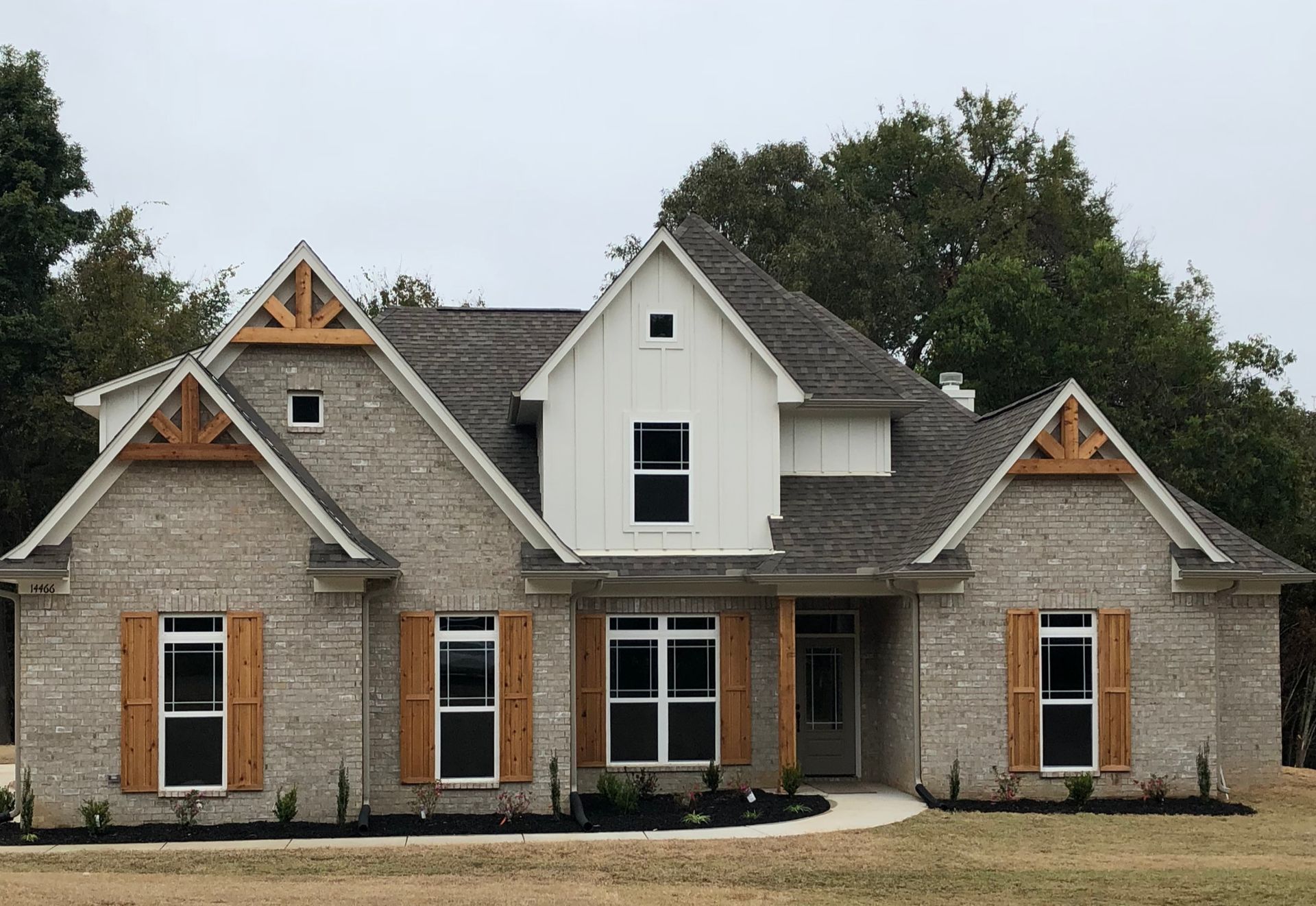 Brick house with light-colored brick exterior, wooden shutters, and decorative wooden roof accents.