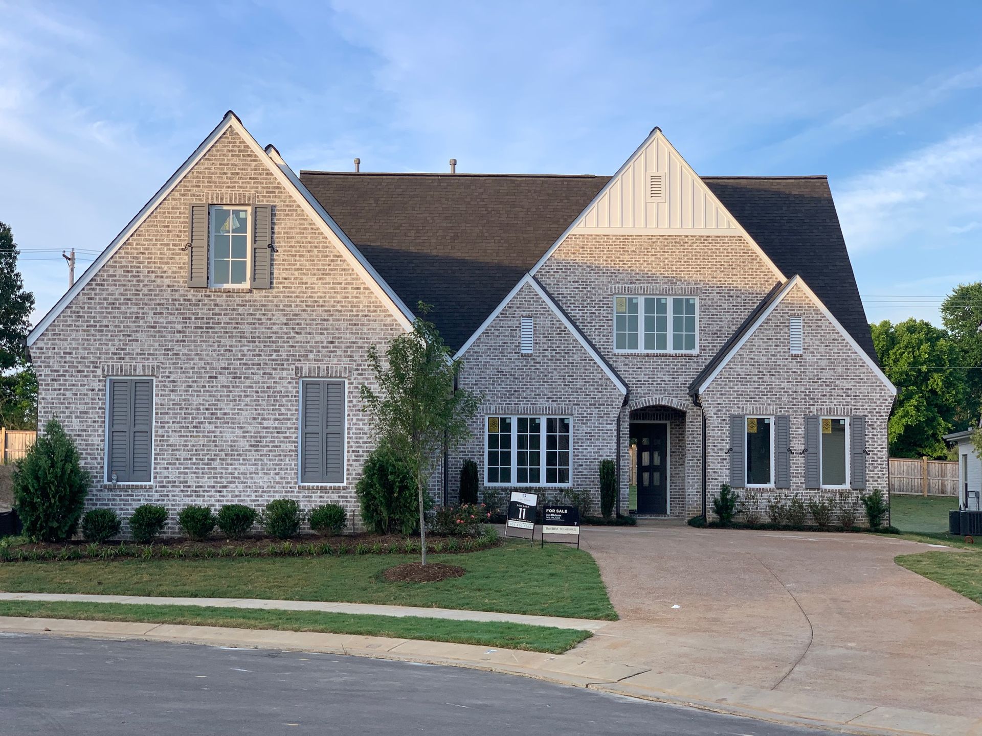 Two-story brick house with dark roof and light gray brick, landscaped front yard, paved driveway.