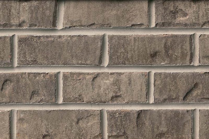 Close-up of a weathered brick wall with dark gray bricks and light gray mortar.