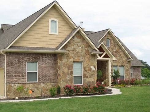 House with brick and stone exterior, tan siding, and green lawn.