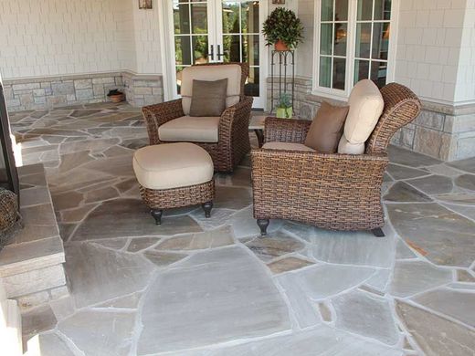 Wicker patio furniture with cushions on a stone patio, beside a fireplace and double doors.