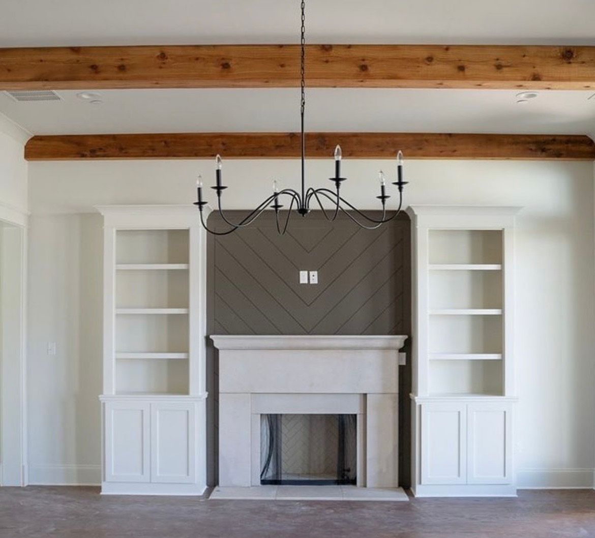 Living room with fireplace, built-in shelves, wood beams, and chandelier.