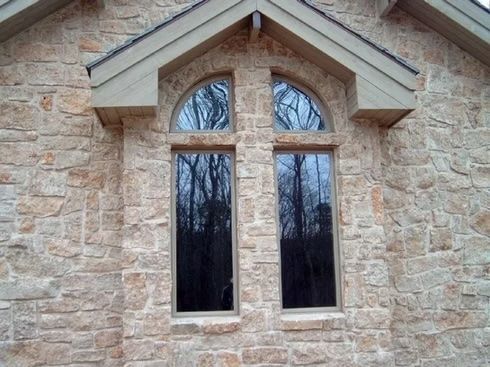 Stone facade with two tall windows, topped by an arched window under a gabled roof.