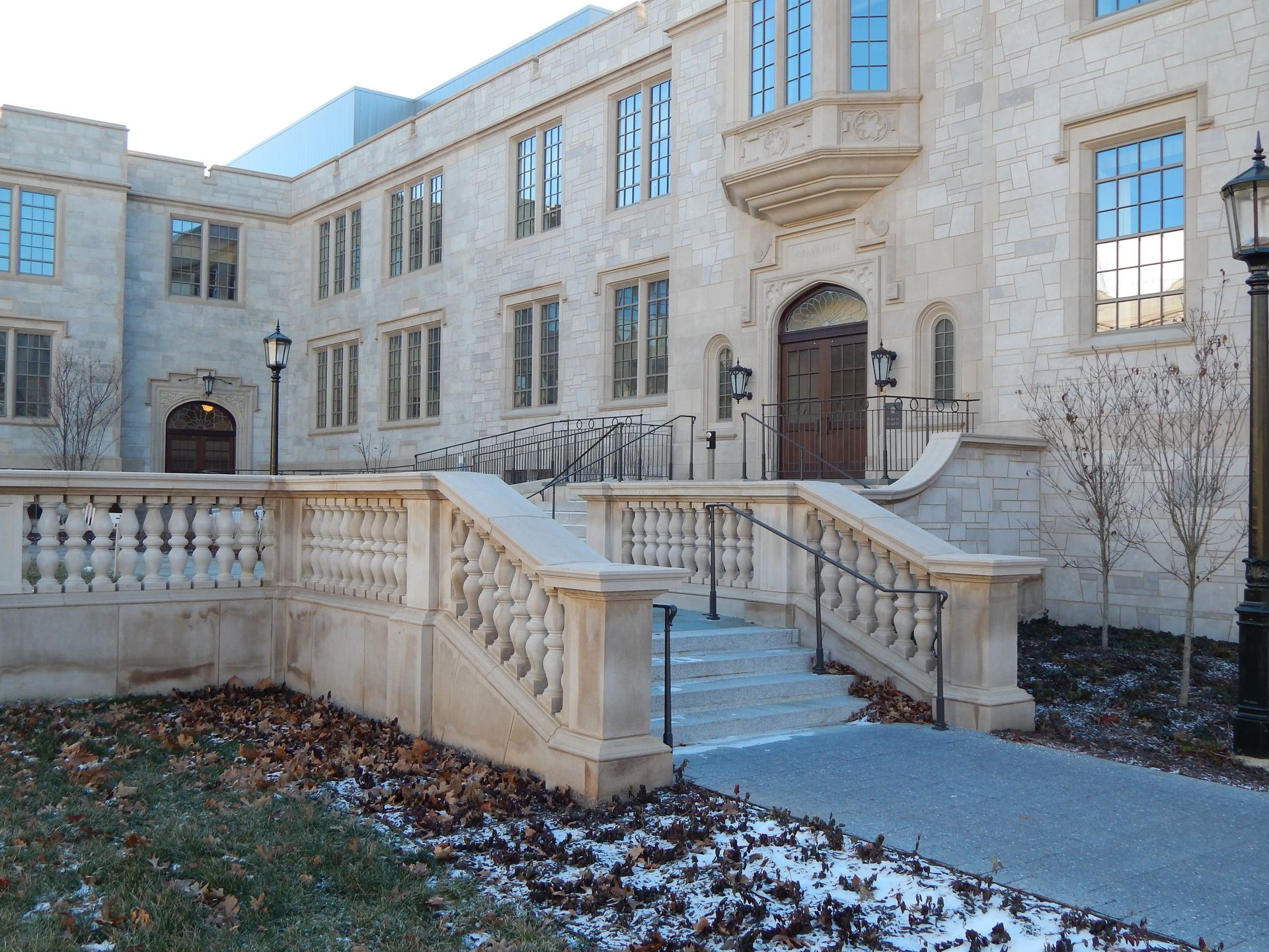 Stone building with stairs leading to a doorway, stone railing. Patches of snow and brown leaves present.