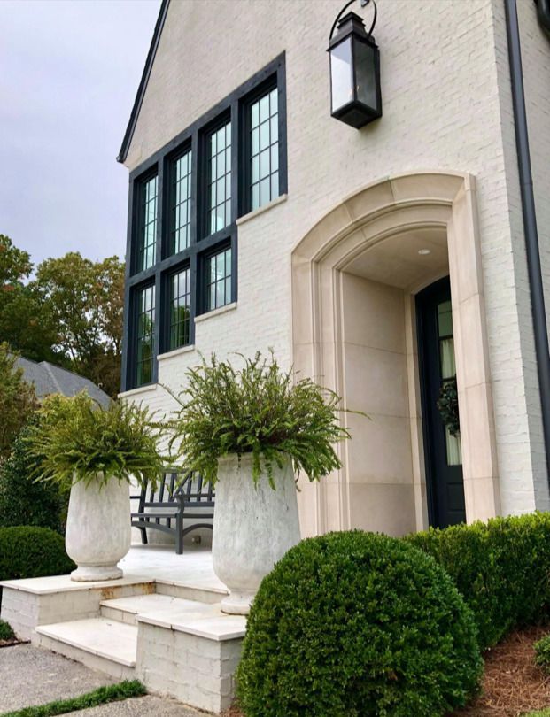 White brick house with black trim, arched entry, and potted ferns.