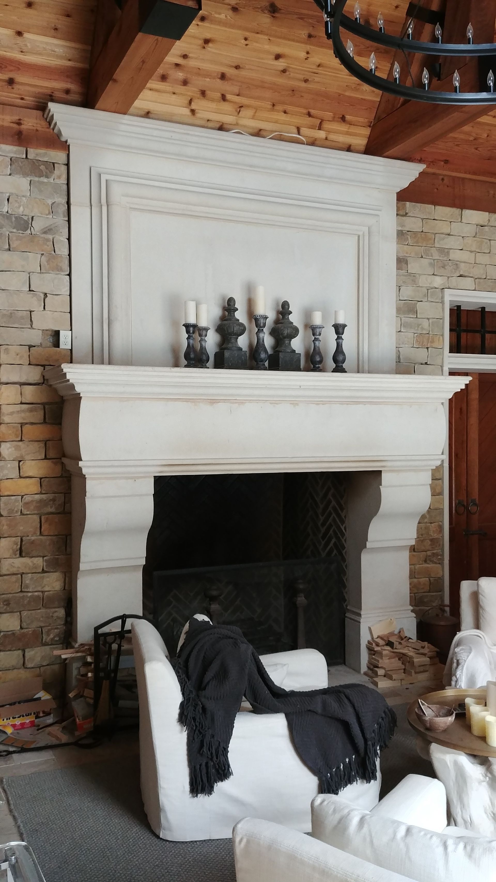 Stone fireplace with candles, set against a stone and wood wall. White chair with black blanket.