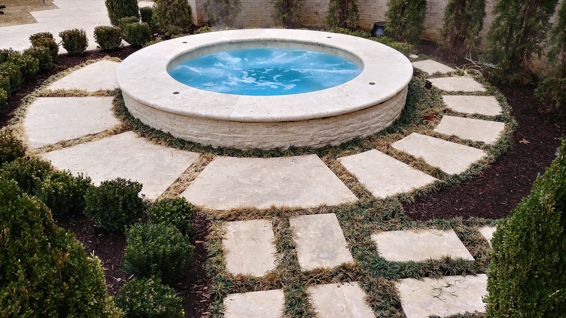 Circular hot tub surrounded by stone pathway and greenery.