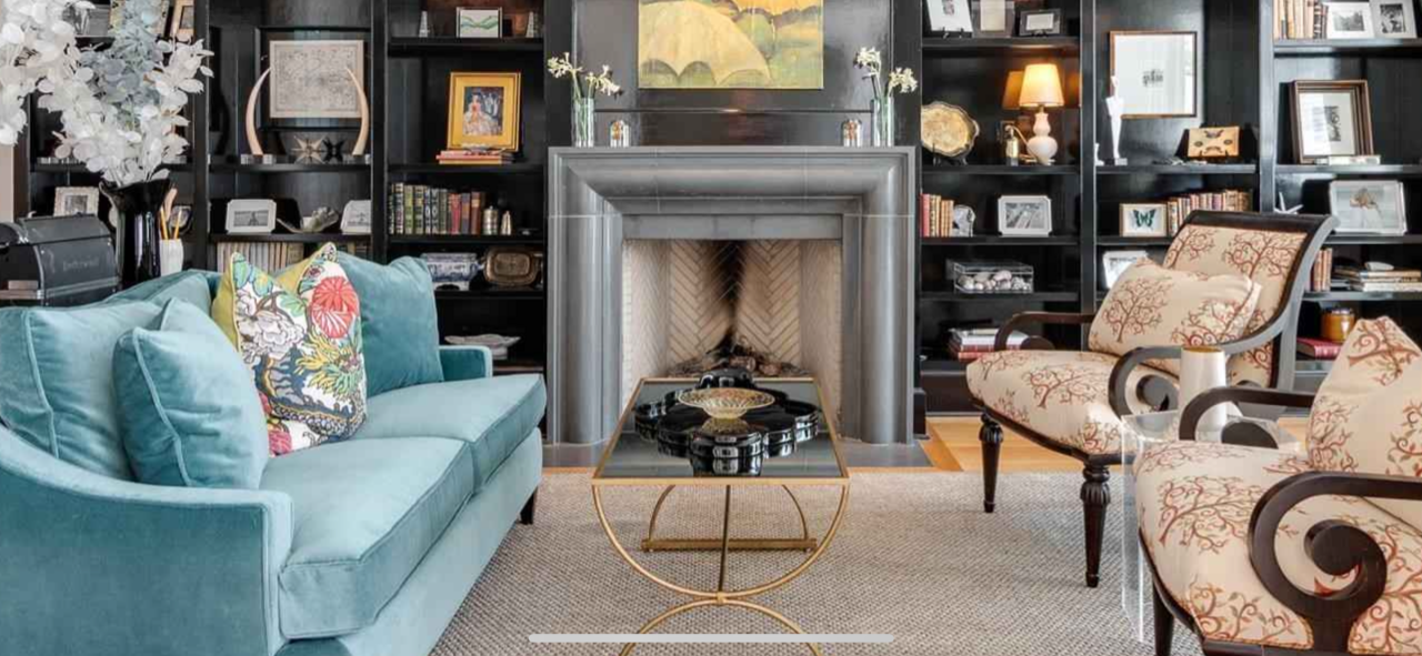 A living room with turquoise sofa, fireplace, bookshelves, and patterned chairs.