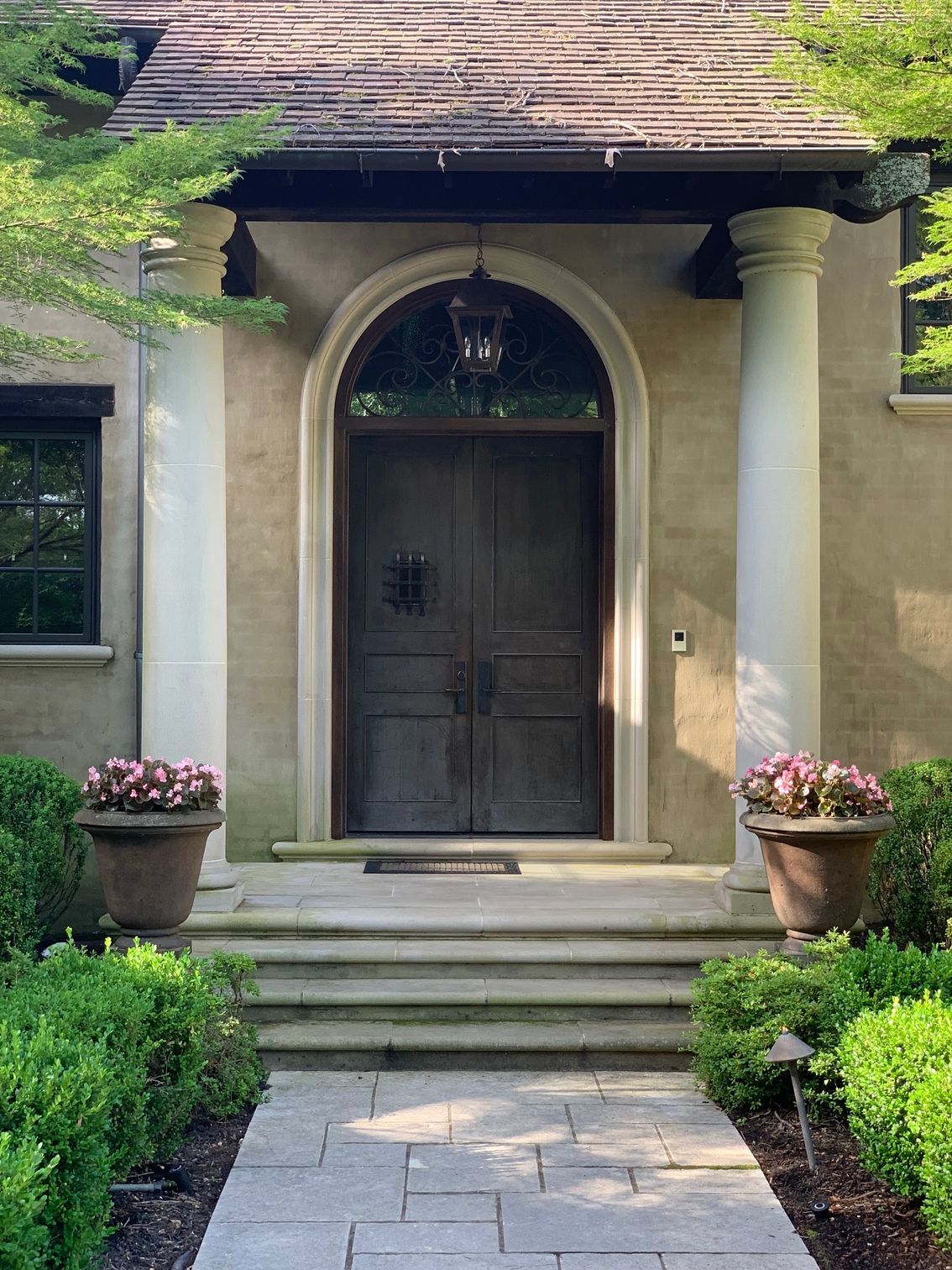 Stone doorway with steps, flanked by columns and potted flowers. Dark wooden doors with a hanging lantern.