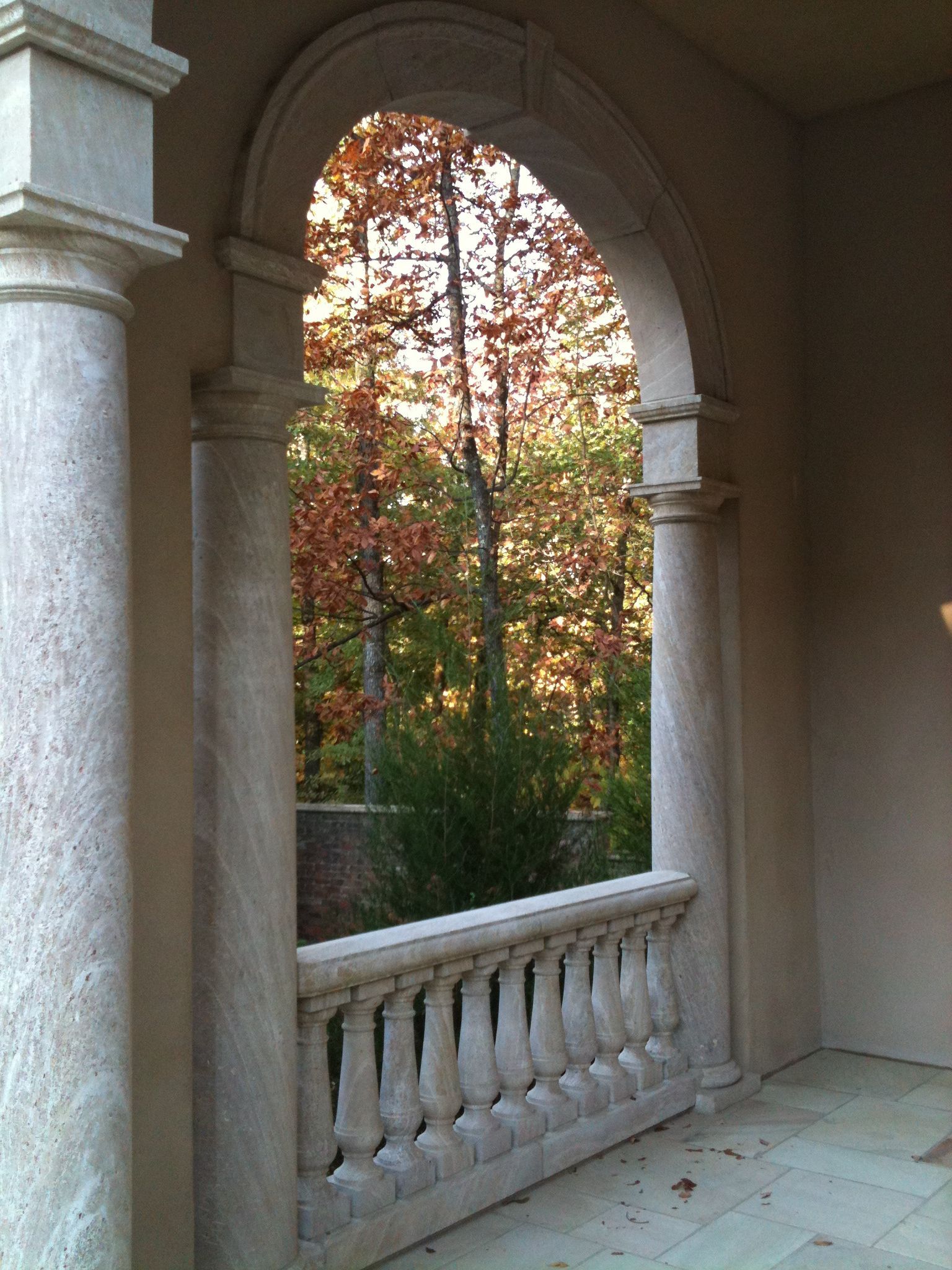 Stone archway framing a view of colorful autumn trees. Balustrade visible below the arch.
