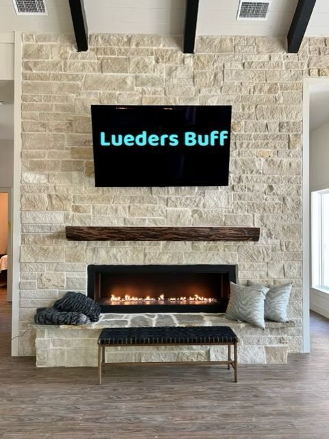 Fireplace with a stone facade, TV above, wooden mantel, and bench.