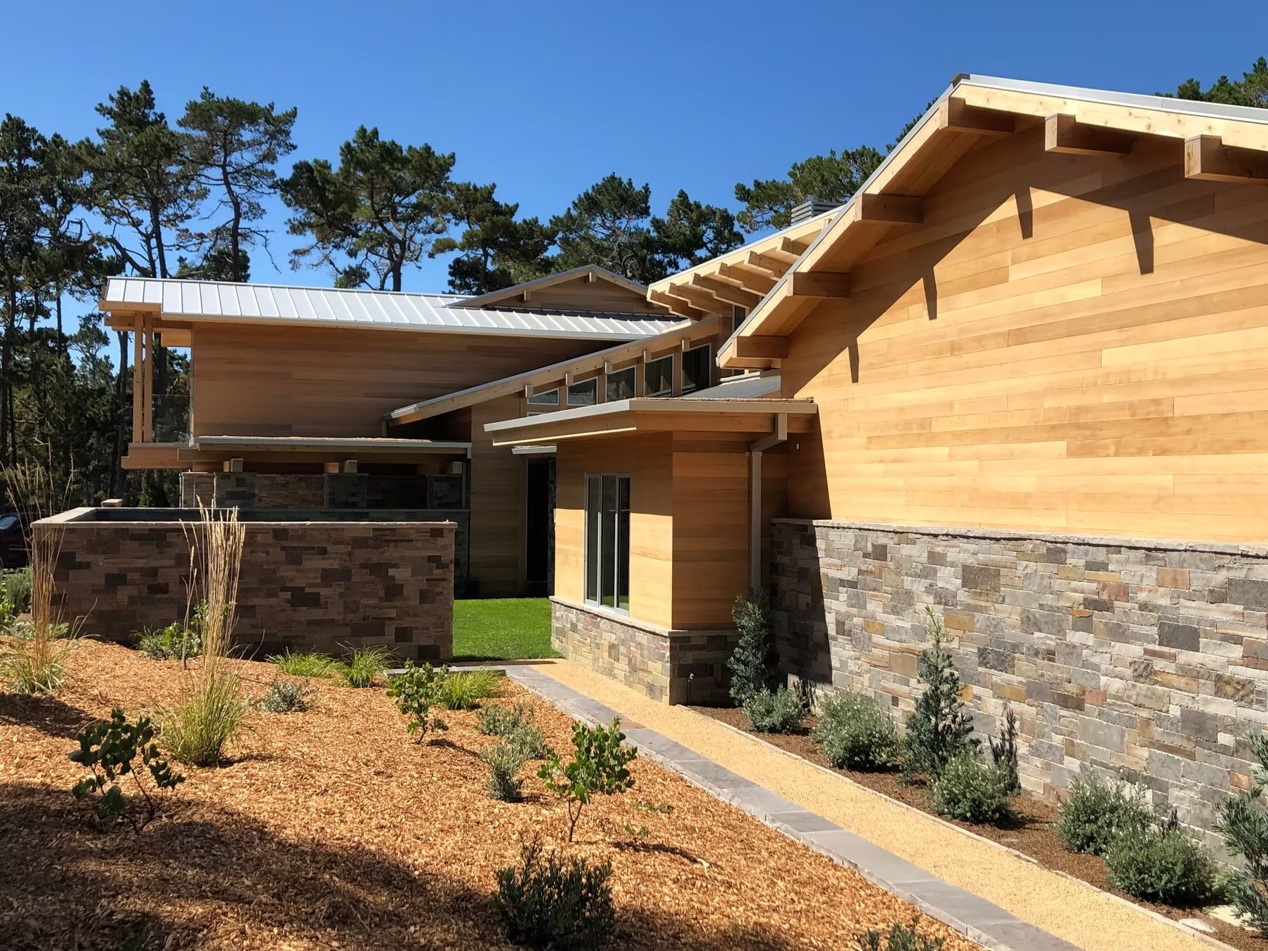 Modern home with light wood siding, stone accents, and a gravel walkway on a sunny day.