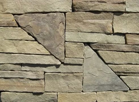 Stone wall with horizontal rectangular and triangular stones, shades of beige and brown.