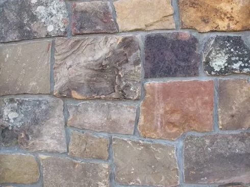 Stone wall composed of various irregularly-shaped, multicolored stones with gray mortar.