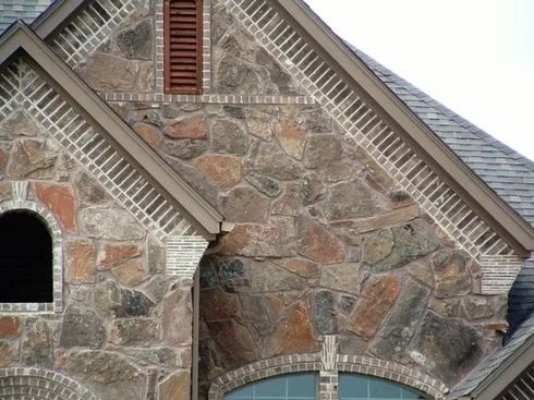 Stone and brick exterior wall of a building with a vent.