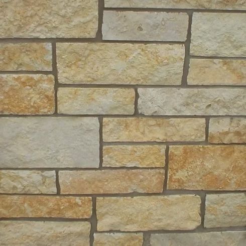 Close-up of a wall made of rectangular, tan-colored stones in a random pattern, with dark grout lines.