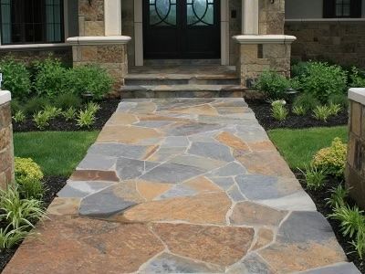 Stone walkway leading to a front door, flanked by greenery and pillars.