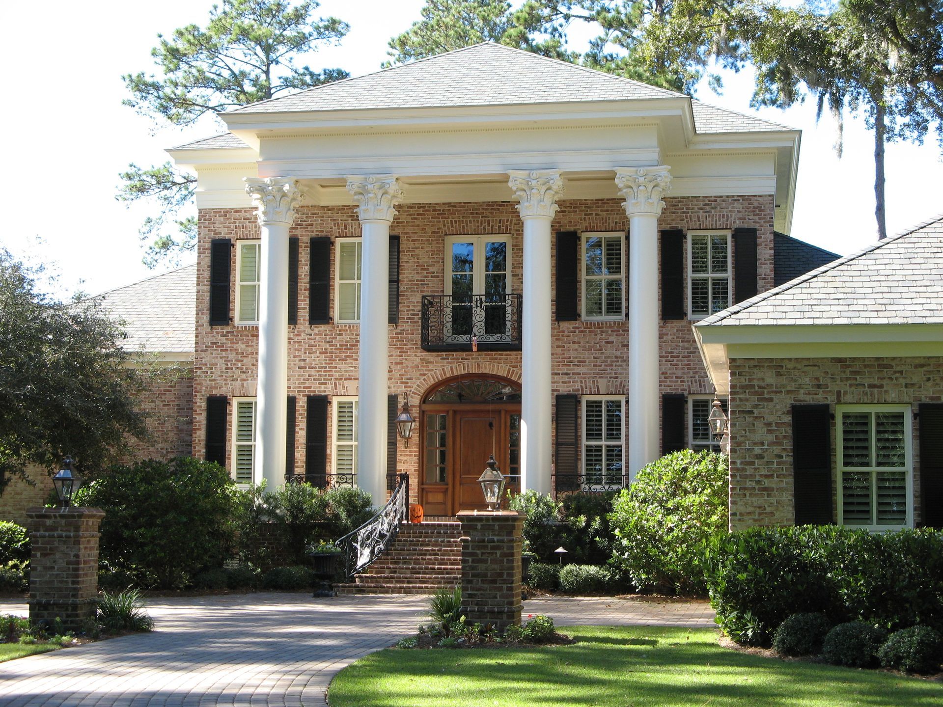 Two-story brick house with white columns, black shutters, and a wooden front door.