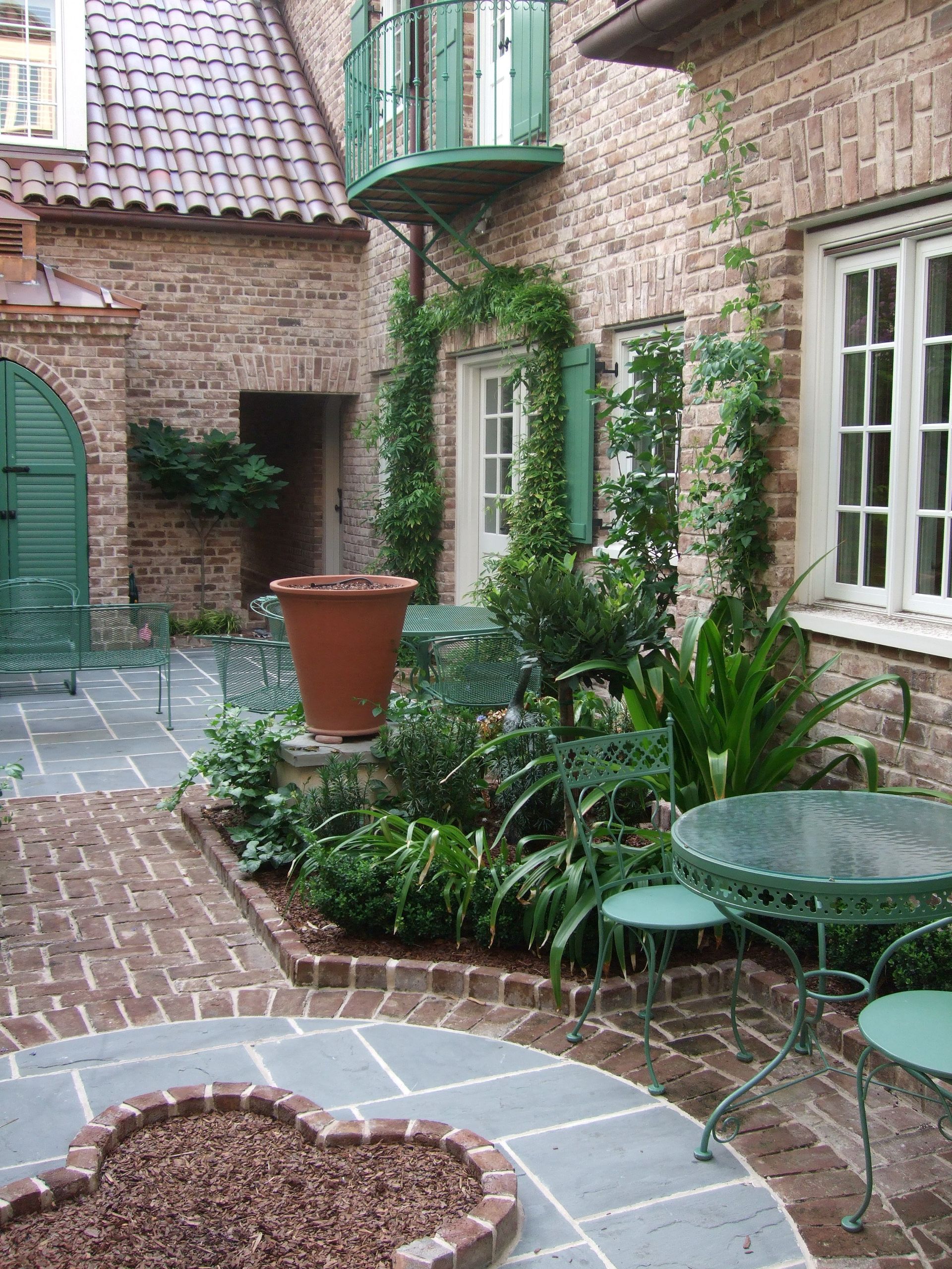 Courtyard with brick and stone, green metal furniture, and climbing plants.
