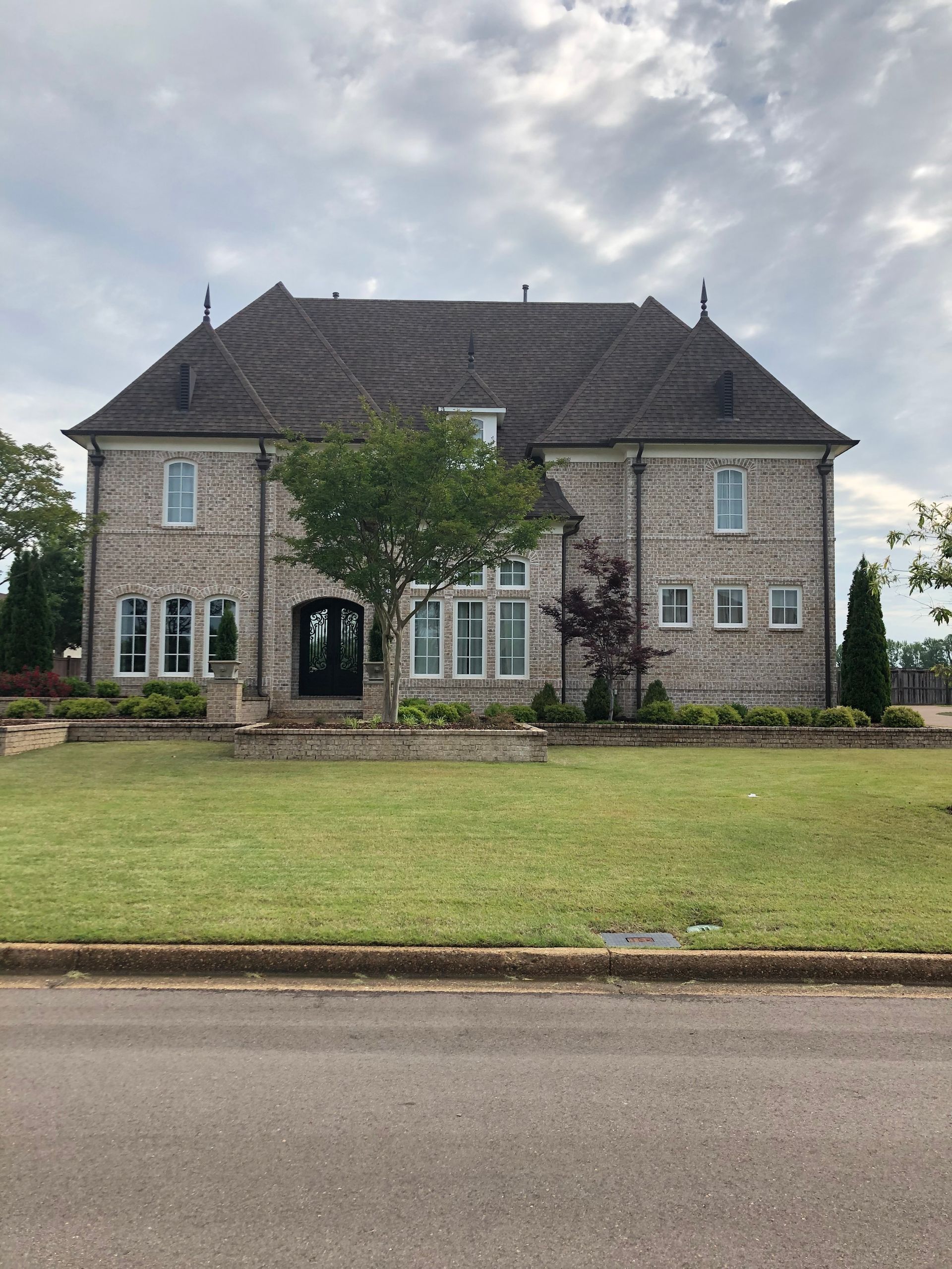 Two-story stone house with a gray roof and manicured lawn under a cloudy sky.