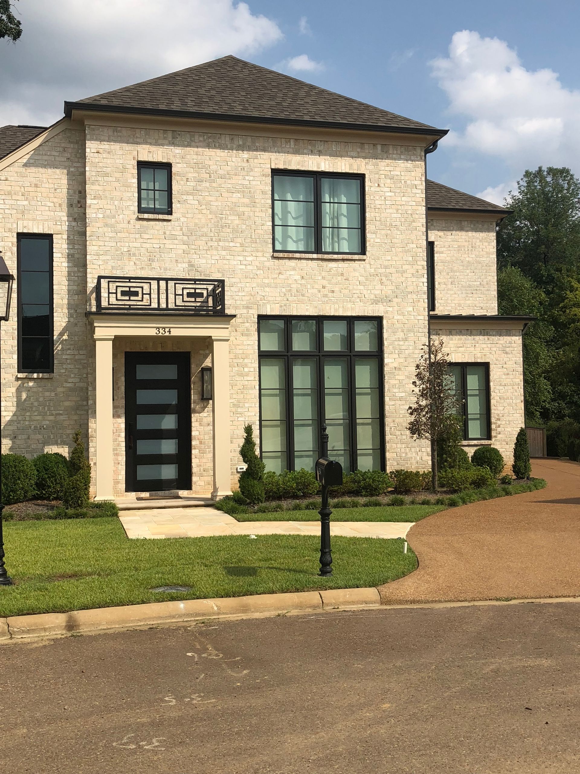 Two-story brick house with black windows and door, manicured lawn and landscaping, gravel driveway.